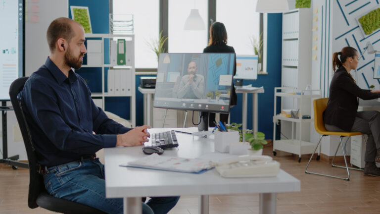 A man working at a desk, using a computer, with a thoughtful expression.